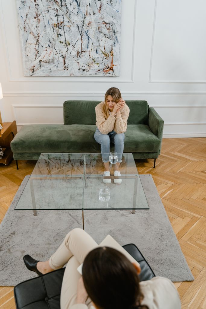 A woman in a therapy session indoors, reflecting emotions with a therapist.